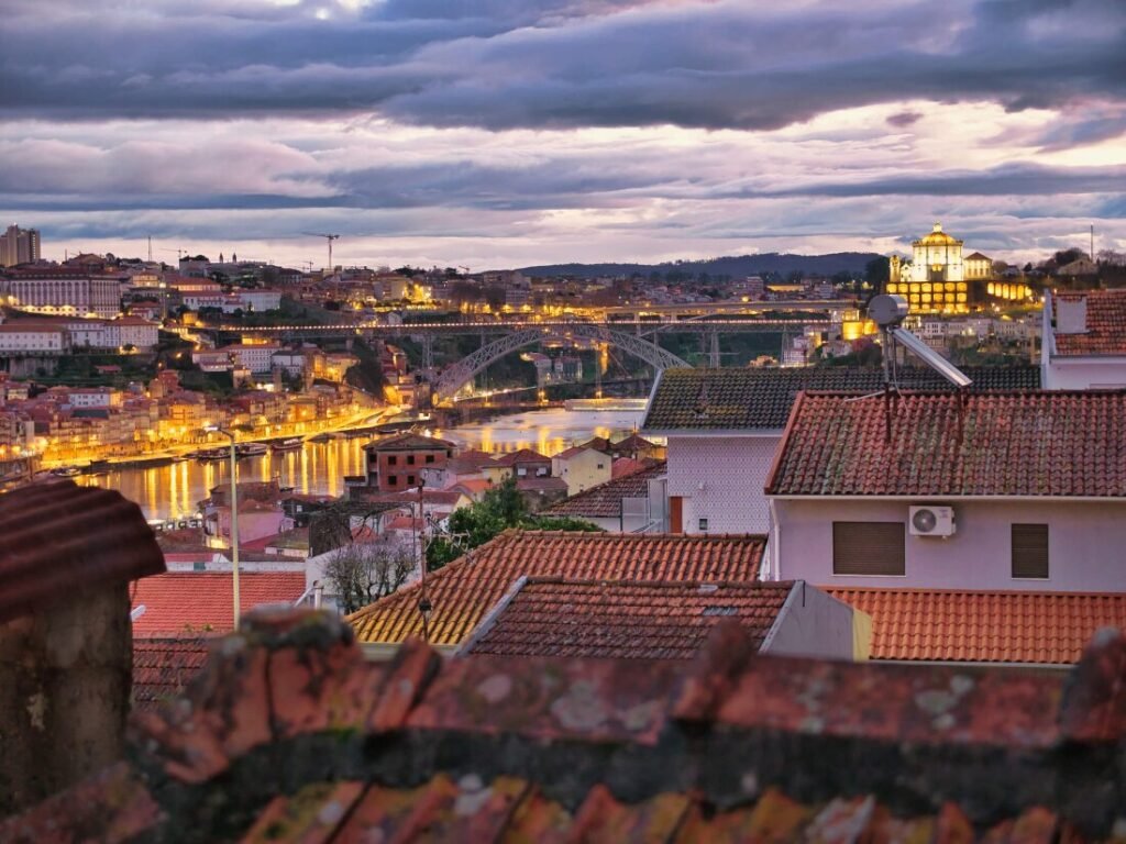 Porto, Portugal: A Slow Travel Guide The historic Dom Luís I iron bridge spanning the Douro River between Porto and Vila Nova de Gaia at twilight under a dramatic, stormy afternoon sky.