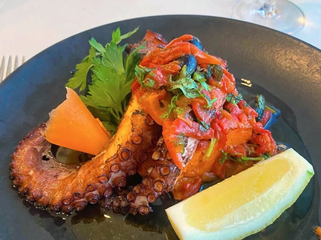 Nazaré: Where the Atlantic Writes Its History | Guide A beautifully plated dish of traditional Portuguese grilled octopus at Pangeia Restaurante in Pederneira, garnished with charred bell peppers, fresh parsley, and a lemon wedge