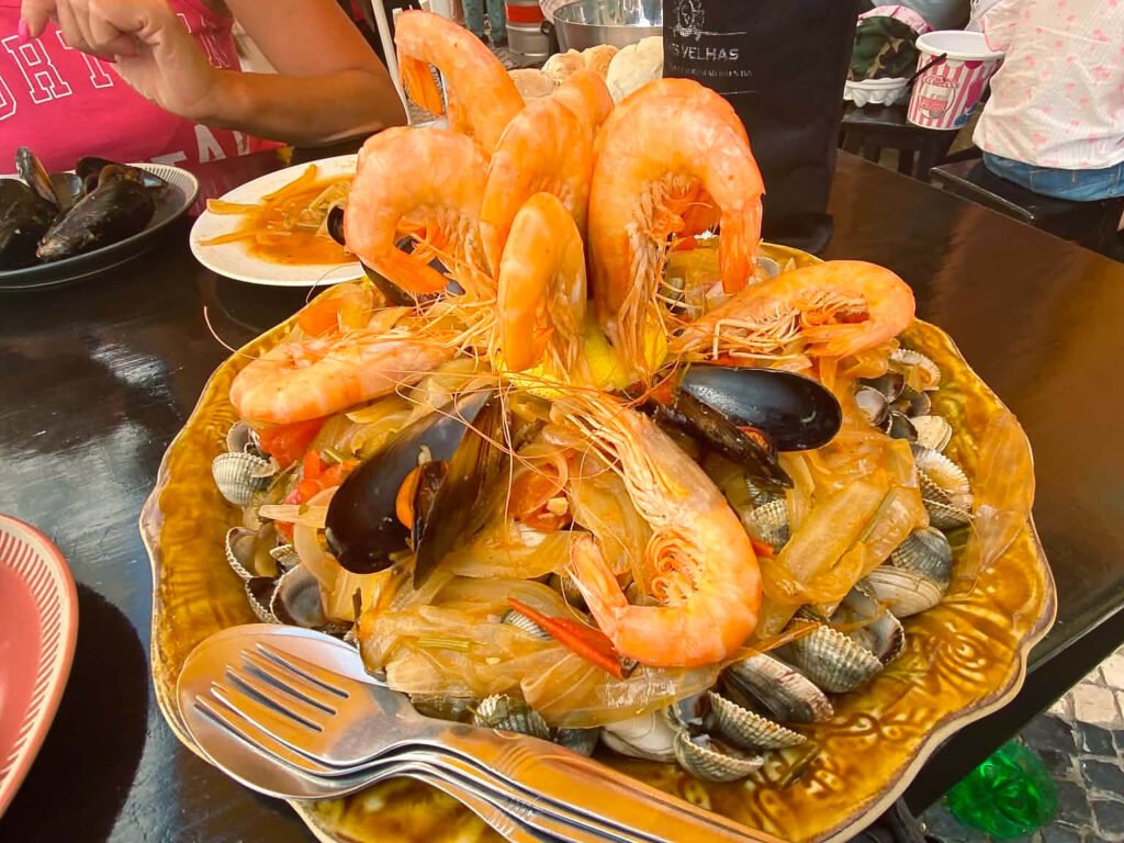 Nazaré: Where the Atlantic Writes Its History | Guide A generous Portuguese seafood platter showcasing large, perfectly grilled prawns arranged on top of a bed of fresh steamed cockles.