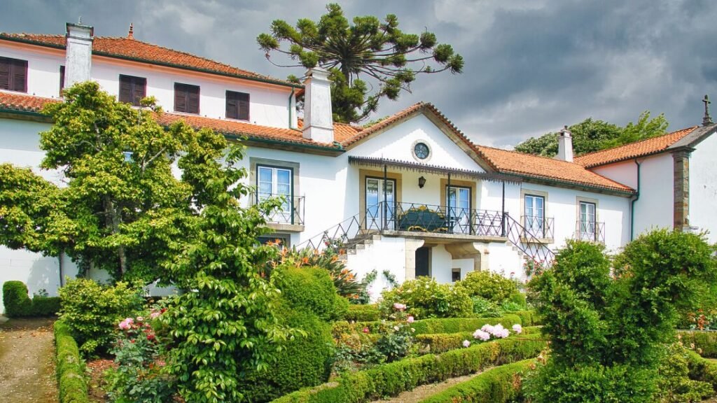 The front facade of the historic white manor house at Quinta de Santa Júlia in Peso da Régua, framed by lush green lawns and mature trees on a bright day.