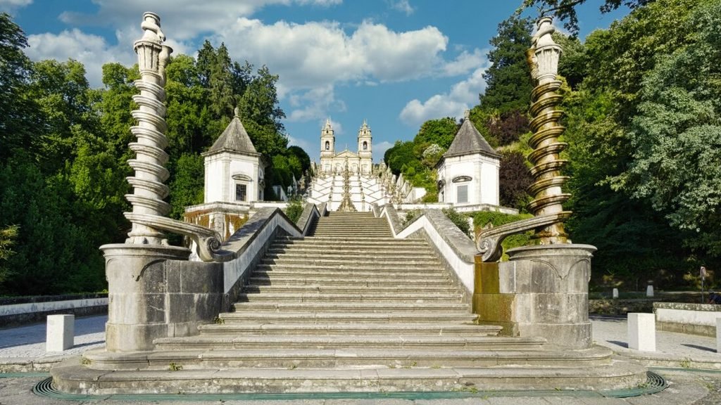 Solo Female Travel in Porto: 3 Day Slow-Travel Itinerary Bright sunny day view looking up the grand symmetrical baroque staircases of the Bom Jesus do Monte sanctuary in Braga Portugal with light clouds in the blue sky