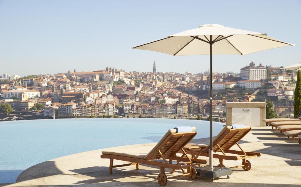 A Guide to the Best Day Tours From Porto An outdoor infinity swimming pool at The Yeatman hotel on a bright sunny day, with the water surface seamlessly blending into a panoramic background view of historic old Porto, including the prominent Clerigos Tower soaring above the terracotta rooftops