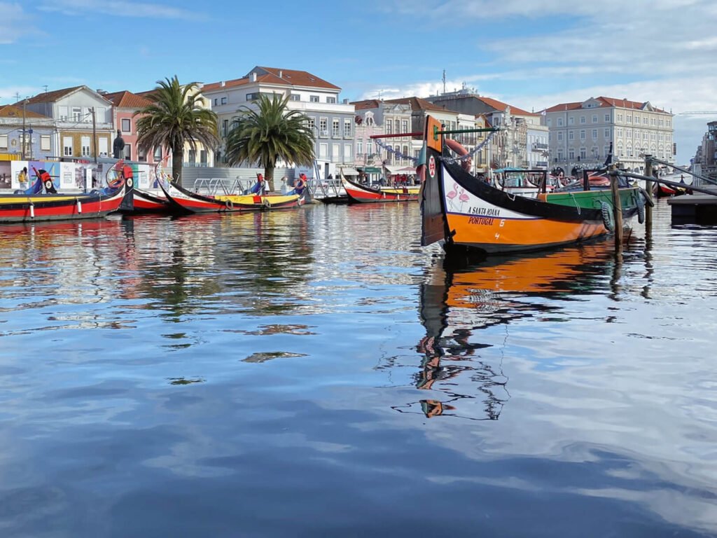 The Poetry of the Silver Coast, Portugal Vibrant and colorful traditional moliceiro boats floating on the calm waters of the central canal in Aveiro under a bright, sunny sky.