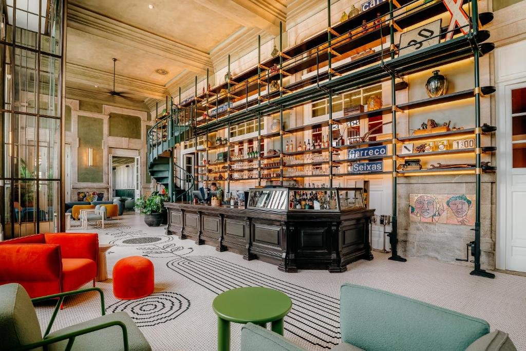 Best Towns in Northern Portugal: A Photographer’s Map The spectacular, design-forward lobby lounge and bar area at Axis Avenida in Viana do Castelo, featuring unique train station inspired architectural scaffolding shelving, a dark wooden service counter, historic town signboards, patterned tile flooring, and vibrant red and green modern armchairs.