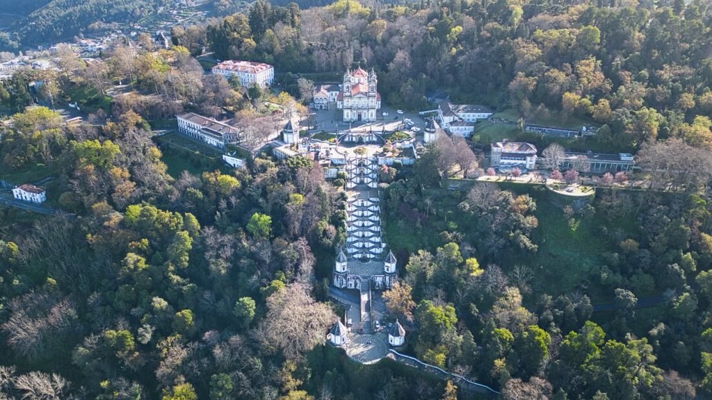A Guide to the Best Day Tours From Porto An aerial drone photograph looking down at the magnificent Bom Jesus do Monte sanctuary in Braga, showcasing the complete zigzagging Baroque staircase and the grand church at the summit surrounded by dense green forest