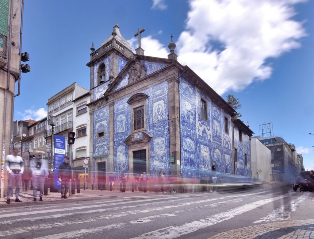 Solo Female Travel in Porto: 3 Day Slow-Travel Itinerary The stunning neoclassical blue and white azulejo tile facade of Capela das Almas church stands brilliantly illuminated under a bright, cloudless sunny sky in downtown Porto.