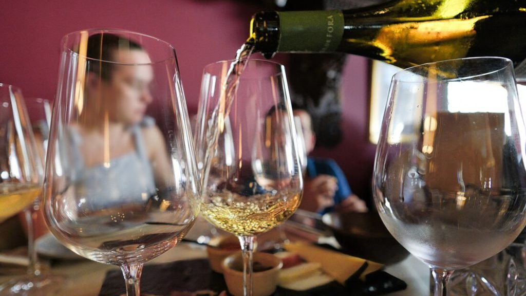 Solo Female Travel in Porto: 3 Day Slow-Travel Itinerary A crisp close-up perspective of chilled Portuguese white wine being poured smoothly into a delicate glass in the foreground at Capela Incomum wine bar.