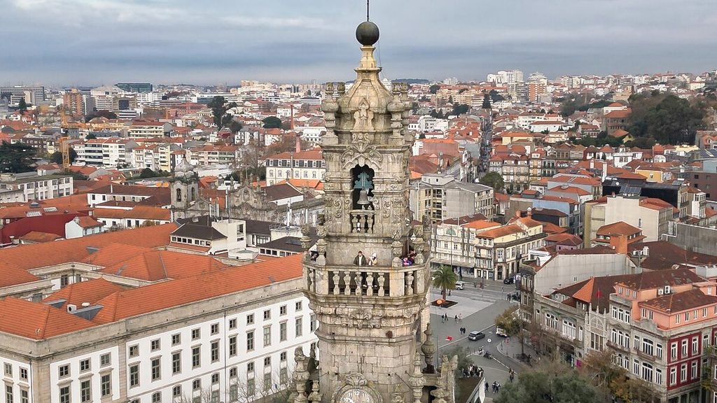 Solo Female Travel in Porto: 3 Day Slow-Travel Itinerary The dramatic granite stone silhouette of Clerigos Tower rises in the center of a sweeping drone perspective, framed by a sea of historic terracotta roofs under a moody, overcast grey sky.