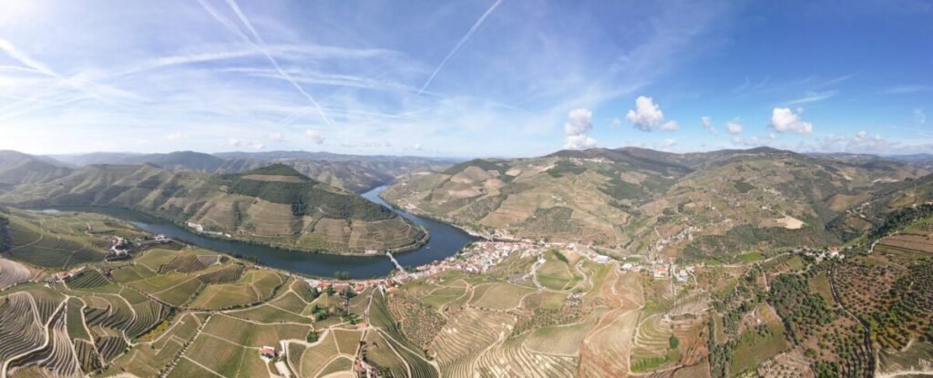 Douro Valley Port Wines: A Portugal Wine Region Guide A sweeping, panoramic drone view looking down on the Douro River as it winds gracefully around steep mountain ridges covered in cascading terraced vineyards.