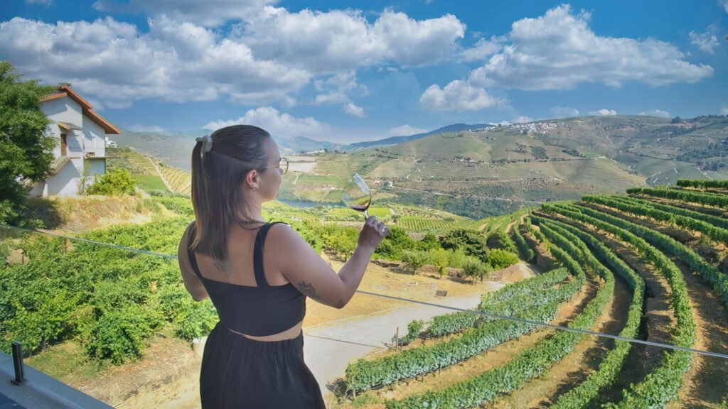 Douro Valley Port Wines: A Portugal Wine Region Guide A traveler holding a glass of wine on a sun-drenched boutique hotel balcony, overlooking the cascading terraced vineyards of the Douro Valley