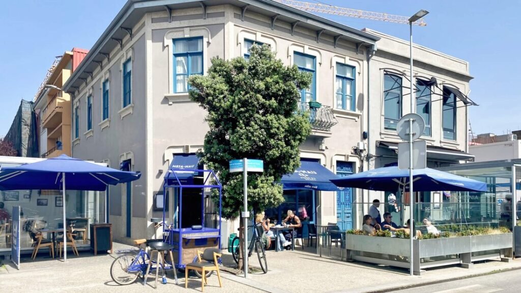 The exterior front facade of Meia-Nau restaurant on a bright, sun-drenched corner in Matosinhos, showcasing its clean modern architecture in the heart of the historic fishing district.