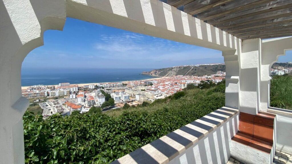 The Poetry of the Silver Coast, Portugal A breathtaking panoramic view looking down from the Miradouro da Pederneira over the crescent golden sand beach and whitewashed seaside village of Nazaré against the deep blue Atlantic Ocean.