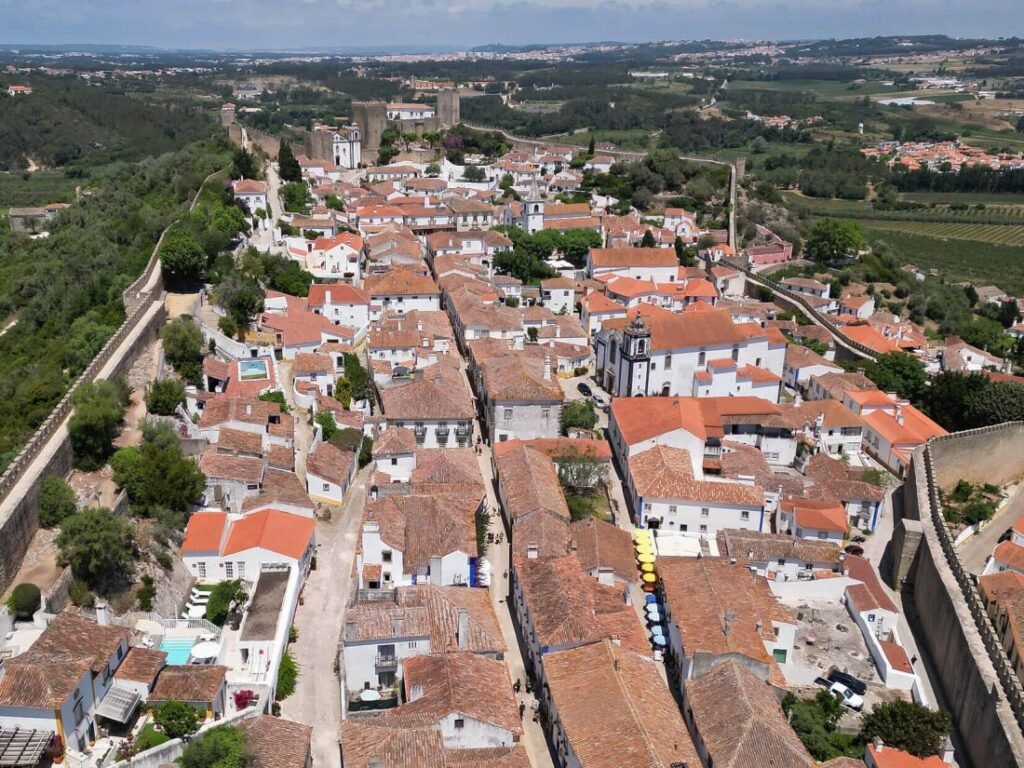 A breathtaking aerial drone photograph of the historic old town and ancient medieval castle walls of Óbidos on a clear, bright sunny day.