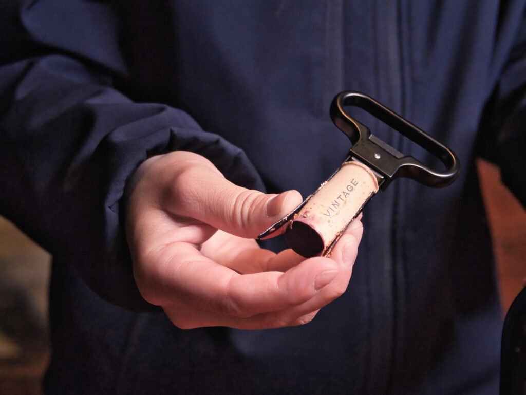 Douro Valley Port Wines: A Portugal Wine Region Guide A close-up shot of a hand holding a wine opener with a traditional cork branded with the word vintage, just extracted from a bottle of aged Port wine