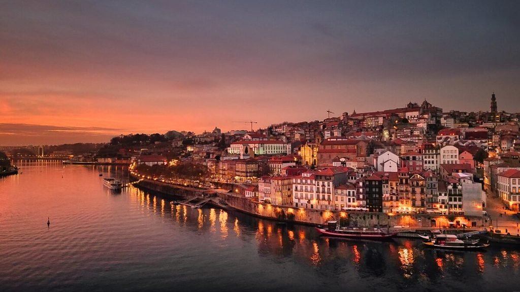 Solo Female Travel in Porto: 3 Day Slow-Travel Itinerary A breathtaking aerial drone perspective captures the winding Douro River and Porto skyline glowing under a dramatic magenta and deep red sunset sky as city lights begin to flicker awake.