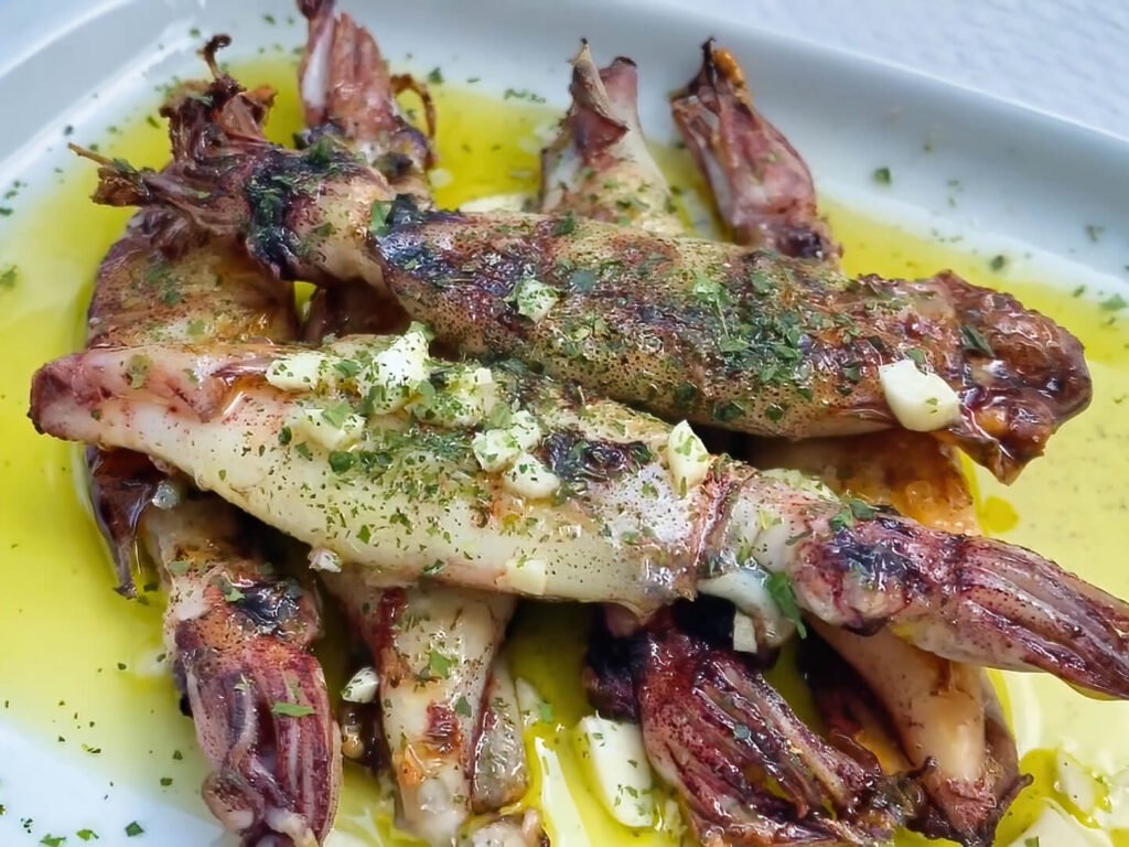A mouthwatering dish of tender, perfectly charred Portuguese grilled calamari glistening with premium olive oil, minced garlic, and fresh parsley herbs.