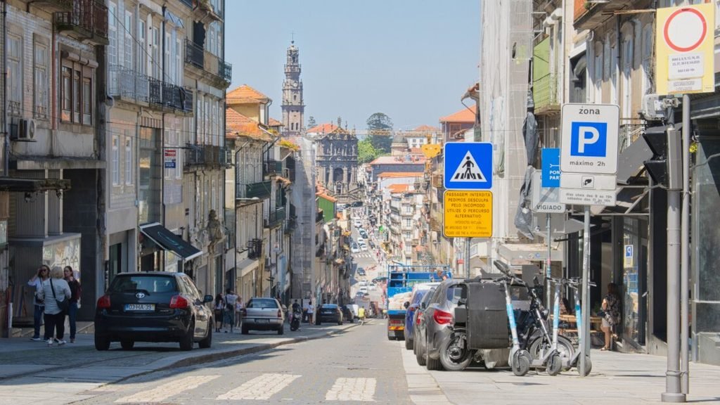 Solo Female Travel in Porto: 3 Day Slow-Travel Itinerary A steep cobblestone view looking down Rua de 31 de Janeiro in central Porto, framing the historic granite silhouette of the Clerigos Tower standing tall in the distant urban skyline.