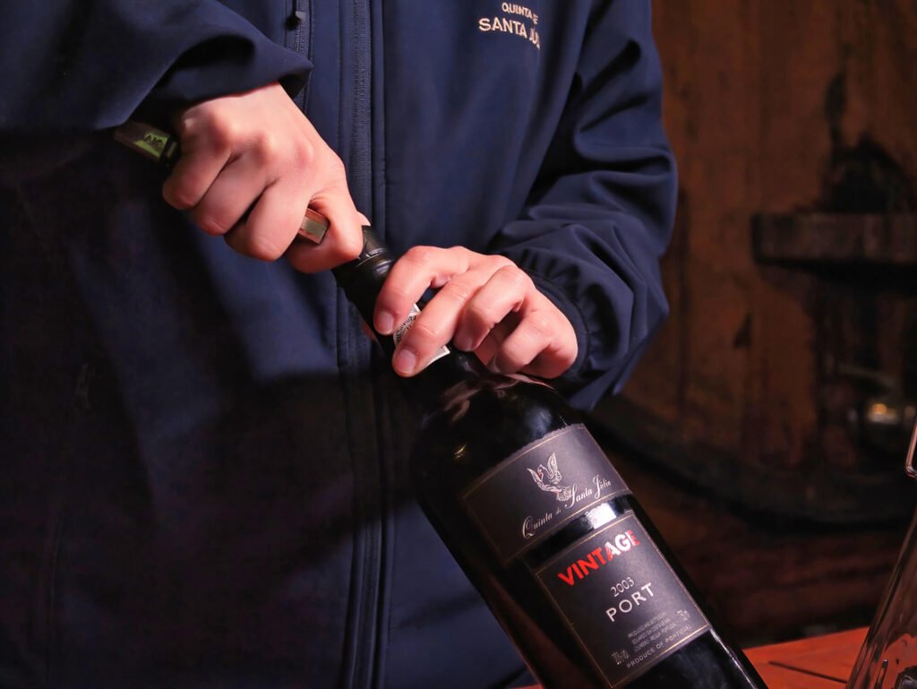 Douro Valley Port Wines: A Portugal Wine Region Guide A dusty, cellared bottle of a classic 2003 Vintage Port wine being opened inside a historic Douro Valley estate.