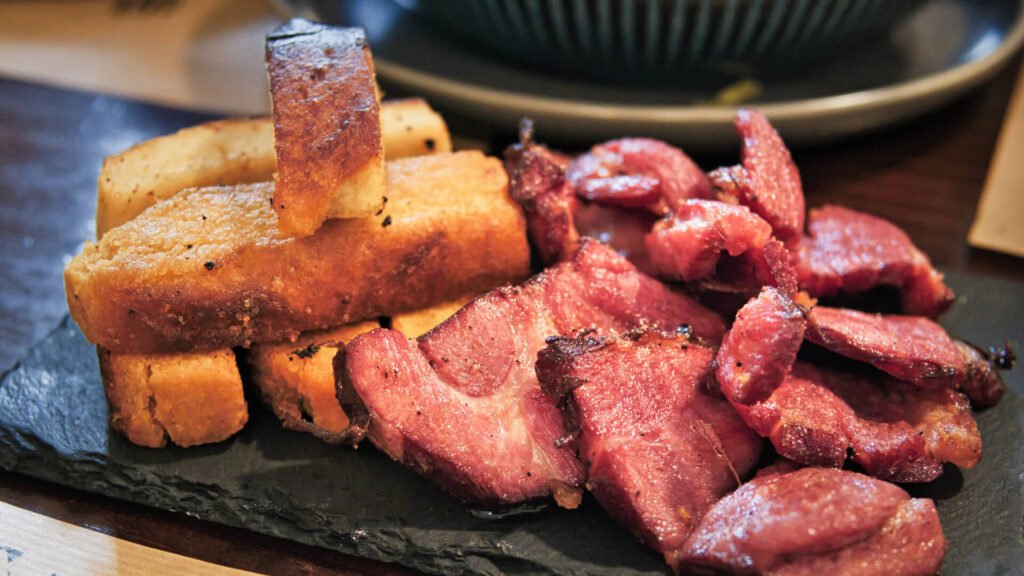 Douro Valley Harvest, Portugal: Best Stays & Dining A rustic plate of traditional Portuguese rojões, showcasing thick-cut seasoned pork chunks and golden cubed potato squares glistening with a rich garlic wine sauce.