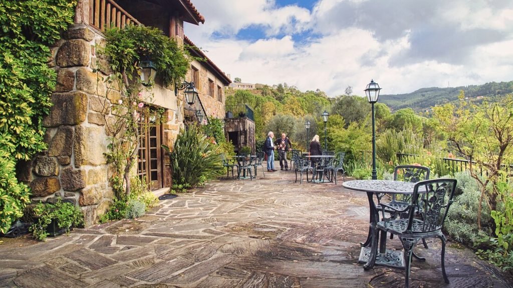 A Guide to the Best Day Tours From Porto An ancient stone manor house in the Vinho Verde wine region, surrounded by lush green trees and dense vegetation, with three people standing in the background talking