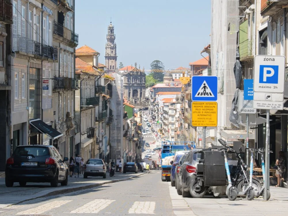 A steep street view looking down Rua de São Bento da Vitória in Porto, Portugal. The iconic Clérigos Tower rises in the background distance.